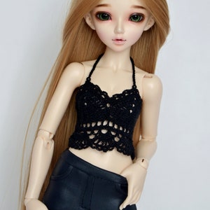 May include: A doll with long blonde hair and green eyes wearing a black crochet halter top and black pants. The doll has a pale complexion and is posed against a white background. The doll's clothing is detailed.