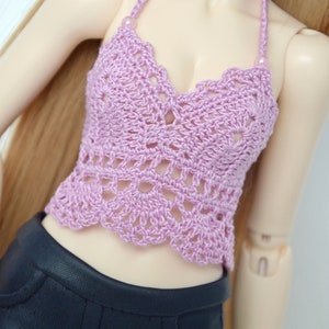 May include: A lavender crochet halter top with a scalloped edge and a delicate openwork design. The top is paired with black pants. The halter straps are adorned with small beads.
