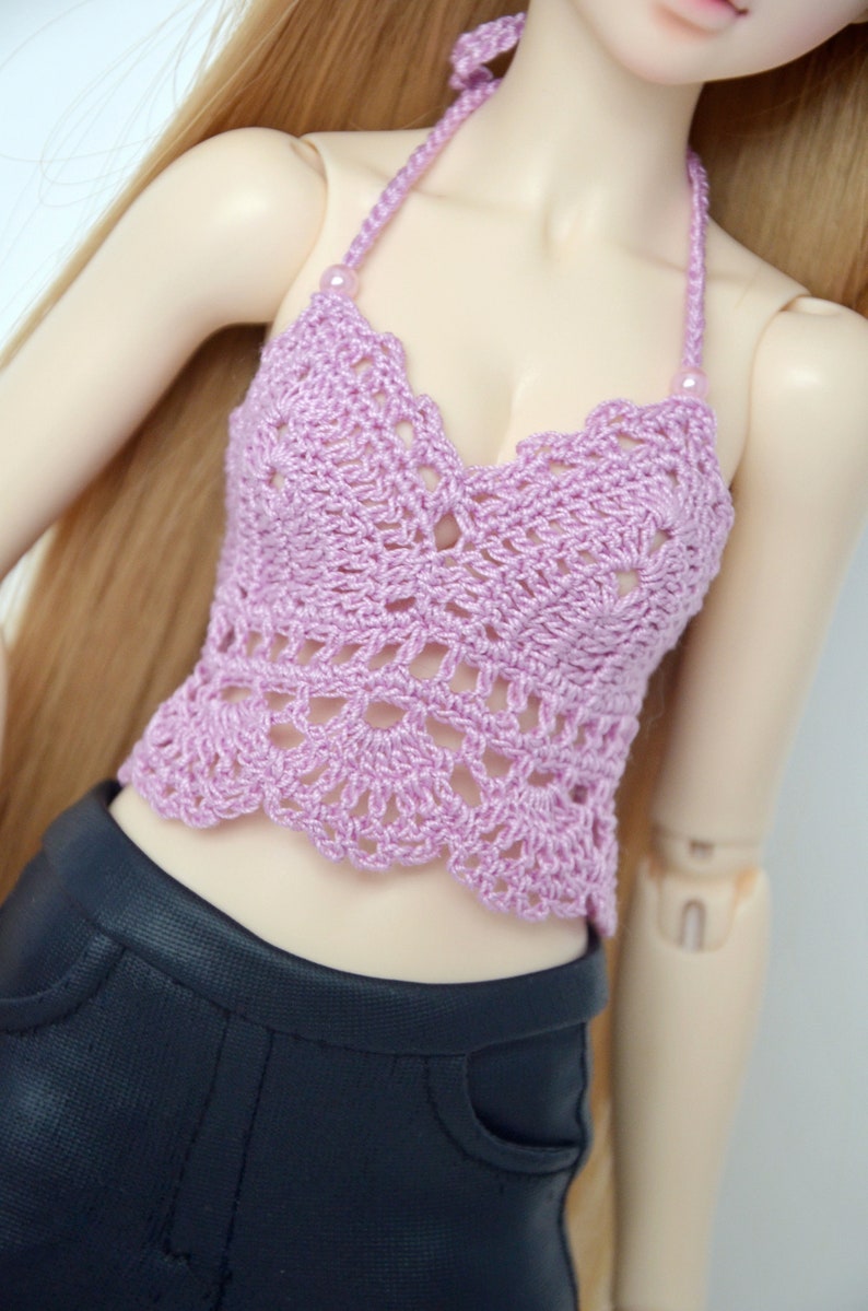 May include: A lavender crochet halter top with a scalloped edge and a delicate openwork design. The top is paired with black pants. The halter straps are adorned with small beads.