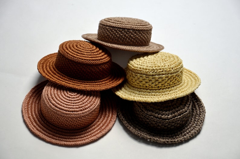 Peut inclure: Cinq chapeaux en crochet de diff&eacute;rentes couleurs et styles, empil&eacute;s les uns sur les autres. Les chapeaux sont faits avec une vari&eacute;t&eacute; de points et de textures, et ils sont tous dans des couleurs neutres.