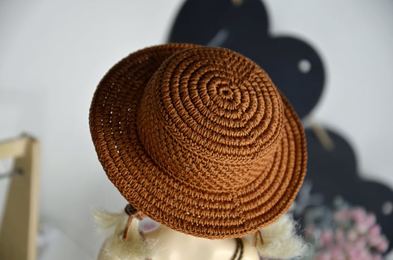 Peut inclure: Un chapeau de soleil en crochet marron &agrave; large bord. Le chapeau est fait d'un fil &eacute;pais et textur&eacute; et a un design simple et classique.