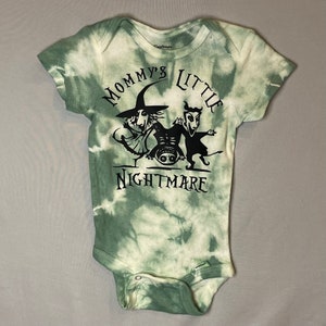 Puede incluir: Un body de bebé de color verde tie-dye con un gráfico negro de personajes de la película "Pesadilla antes de Navidad" y el texto "Mommy's Little Nightmare".