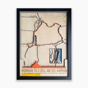 Könnte beinhalten: Eine gerahmte 3D-topografische Karte der Ironman 70.3 Zell am See-Kaprun Strecke. Die Karte zeigt geschichtete Holztexturen, eine hervorgehobene orangefarbene Route, blaue Wasserelemente und ein Höhenprofil mit dazugehörigem Text.