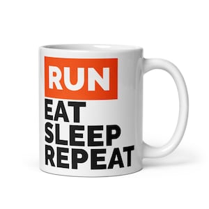May include: White ceramic mug with the words "RUN" in white on an orange rectangle, and the words "EAT SLEEP REPEAT" in black below. The mug has a white handle and is designed for hot beverages.