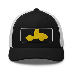 May include: A black and white trucker hat with a yellow embroidered silhouette of a road roller in a white rectangle.
