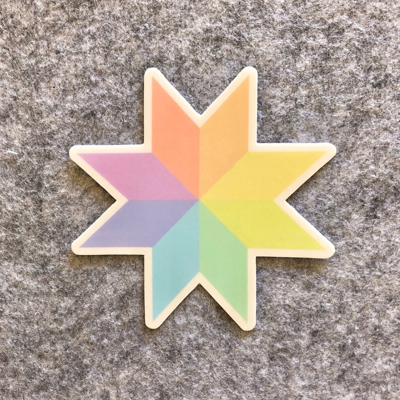 May include: A colorful sticker in the shape of an eight-pointed star. The star is divided into eight sections, each a different pastel color: orange, yellow, green, blue, purple, and pink. The sticker has a white border and is placed on a gray surface.