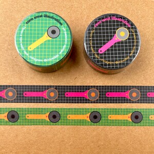 May include: Two rolls of washi tape with a rotary cutter design. One roll is green with a yellow cutter, the other is black with a pink cutter. Below are two strips of washi tape, one with a green background and yellow cutters, the other with a black background and pink cutters.