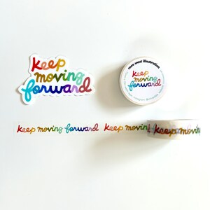 May include: A sticker, washi tape roll, and washi tape strip featuring the phrase "keep moving forward" in rainbow hues. The sticker is a die-cut shape. The tape roll and strip display the same text. The tape roll has extra text.