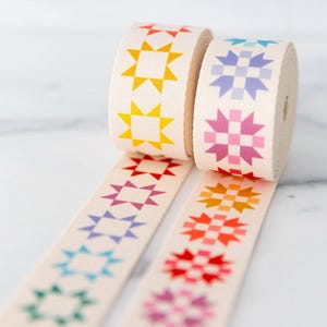 May include: Two rolls of cream-colored ribbon with a repeating star pattern in various colors. The stars are in shades of yellow, orange, red, pink, purple, blue, and green. The ribbon is unspooled, revealing the star pattern.