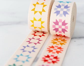 May include: Two rolls of cream-colored ribbon with a repeating star pattern in various colors. The stars are in shades of yellow, orange, red, pink, purple, blue, and green. The ribbon is unspooled, revealing the star pattern.