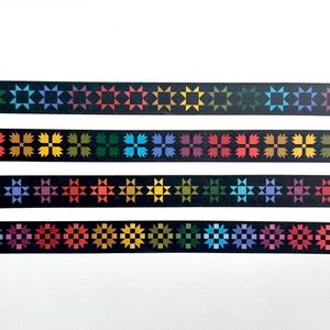 May include: Four horizontal strips of black washi tape featuring repeating geometric star and flower patterns in a vibrant rainbow of colors including red, orange, yellow, green, blue, and purple. Each strip displays a unique repeating motif.