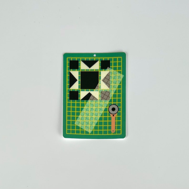 May include: A green and yellow cutting mat with a geometric design, a clear ruler, and a rotary cutter. The mat features a black and white quilt block design, perfect for quilting and sewing projects.