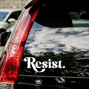 May include: A black car with a white vinyl sticker that says "Resist." on the back window.