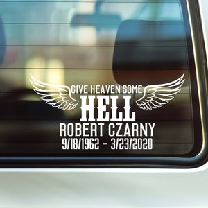 May include: A white car with a sticker on the back window that says "Give Heaven Some Hell Robert Czarny 9/18/1962 - 3/23/2020". The sticker features a pair of white angel wings.
