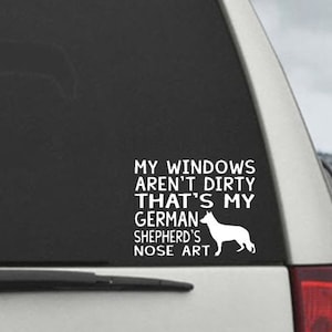 May include: White vinyl decal applied to a car window. The decal features the text "MY WINDOWS AREN'T DIRTY THAT'S MY GERMAN SHEPHERD'S NOSE ART" and a silhouette of a German Shepherd dog.