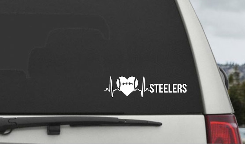 K&ouml;nnte beinhalten: Ein wei&szlig;er Vinyl-Aufkleber mit einem herzf&ouml;rmigen Design, das einen Fu&szlig;ball enth&auml;lt. Das Herz ist von einer stilisierten Herzschlaglinie umgeben. Der Text "STEELERS" befindet sich rechts vom Herzen.
