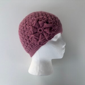 May include: A mauve crocheted beanie with a large crocheted flower on top.