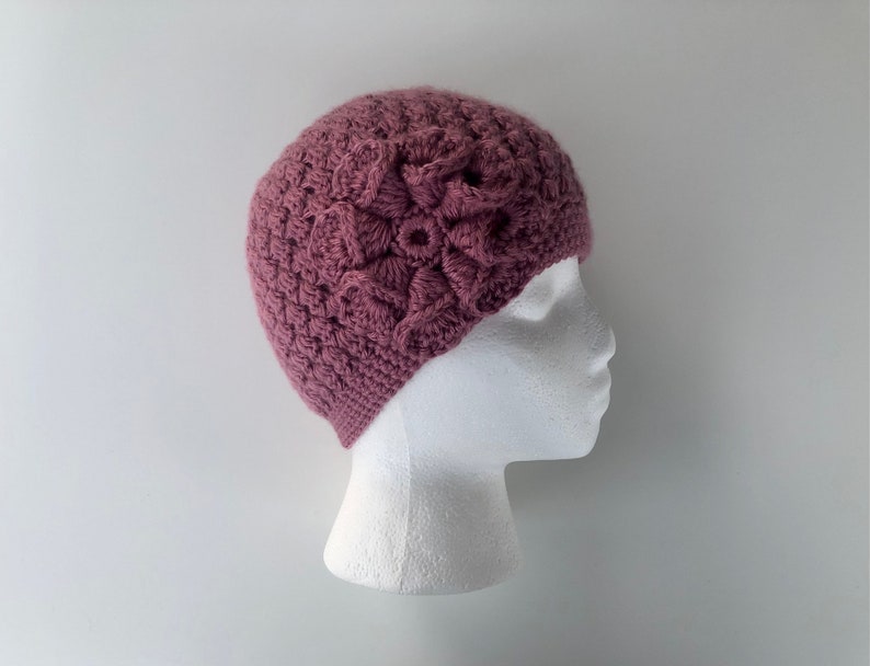 May include: A mauve crocheted beanie with a large crocheted flower on top.