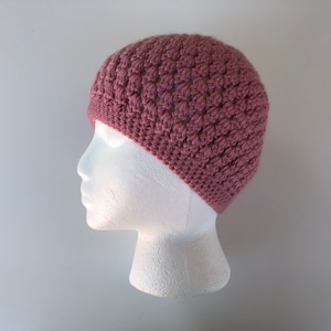 May include: A pink crocheted beanie hat on a white mannequin head.