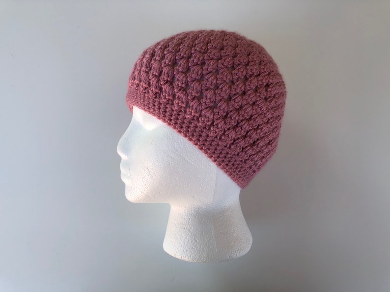May include: A pink crocheted beanie hat on a white mannequin head.