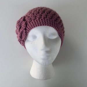 May include: A mauve crocheted beanie with a flower detail on the side.