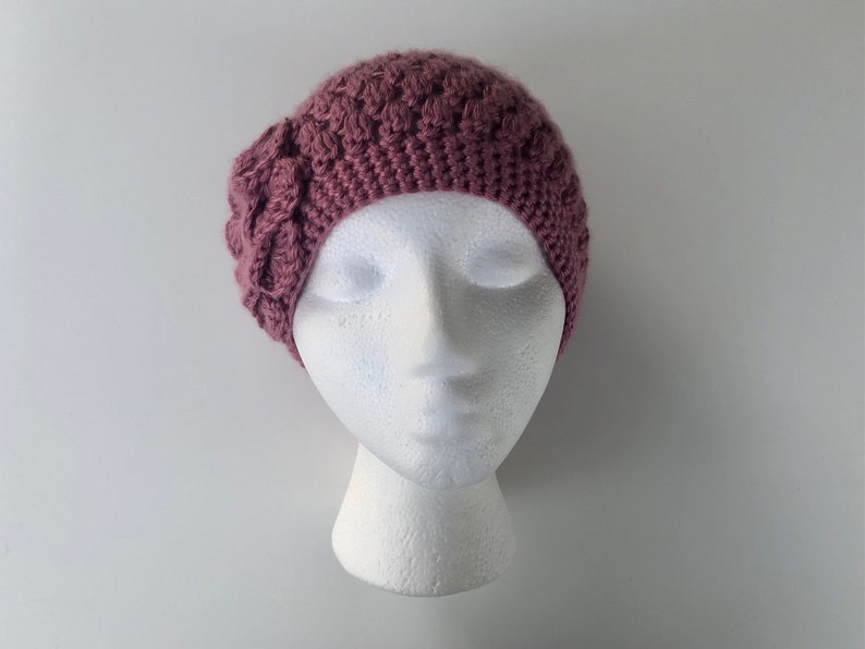 May include: A mauve crocheted beanie with a flower detail on the side.