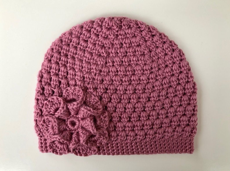 May include: A pink crocheted beanie with a flower design on the side.