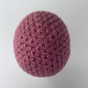 May include: A close-up of a crocheted beanie in a dusty rose color. The beanie is made with a textured stitch pattern.