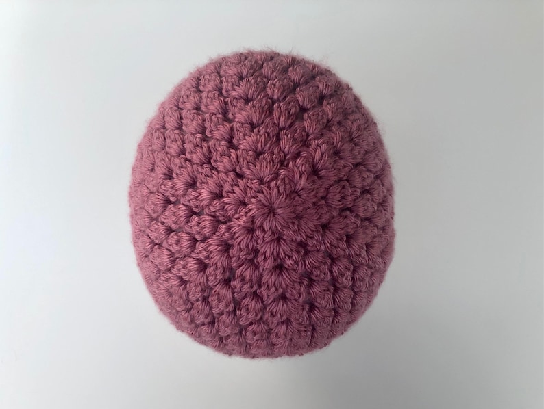 May include: A close-up of a crocheted beanie in a dusty rose color. The beanie is made with a textured stitch pattern.