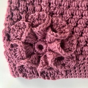 May include: Close-up of a crocheted flower design in a deep pink color. The flower is made up of multiple layers of crocheted stitches, creating a textured and dimensional look.