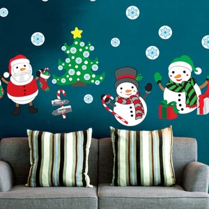 May include: A gray couch with two striped pillows in front of a teal wall with Christmas decorations. The decorations include a Christmas tree, Santa Claus, and two snowmen. The text "Merry & Bright" is on a sign.