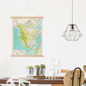 May include: A vintage map of North America hanging on a wall in a dining room. The map is framed with a wooden dowel rod and has a light blue background with green and brown lines representing geographical features. The map is titled "NORTH AMERICA" and includes a scale bar and a legend.
