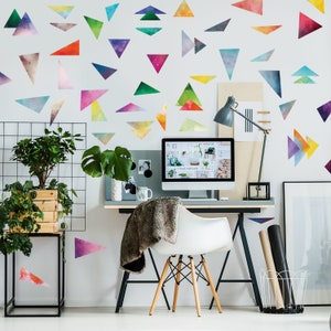 May include: A home office workspace with a white desk and a white chair. The wall is decorated with colorful watercolor triangle stickers. A computer monitor is on the desk with the word "inspirations" displayed on the screen. There are plants and a lamp on the desk.