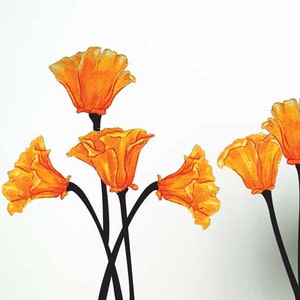May include: Wall decals featuring watercolor-style orange flowers with black stems. The floral art is displayed against a white wall, with a modern chair and a potted plant in the room. The flowers add a touch of nature to the interior.