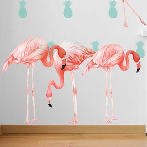 May include: Pink flamingo wall decals with a tropical pineapple design. The decals are on a white wall with a white table and a pink rug.