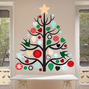 May include: A wall decal of a stylized Christmas tree with a black trunk and branches. The tree is decorated with red, green, and blue ornaments, hearts, snowflakes, and birds. A beige star tops the tree. The decal is on a beige wall.