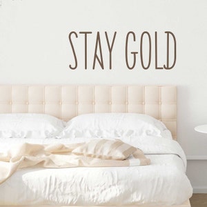 May include: A white upholstered headboard with a brown vinyl decal that reads "STAY GOLD" above it.