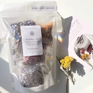 May include: A clear plastic bag filled with four small bags of dried herbs labeled "Herbal Kit, Herbal Ceremony, Rose-Lavender-Chamomile, Calendula-Rosemary-Sage, Cornflower-Jasmine". The text "Heal Love Invoke" is printed on the top of the bag. The bag is sitting on a white surface with a small bouquet of dried flowers.