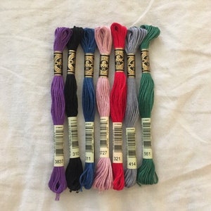 Images shows examples of the embroidery thread color options. From left: Purple, Black, Blue, Pink, Red, Gray, Green.