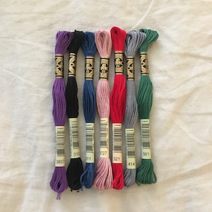 Images shows examples of the embroidery thread color options. From left: Purple, Black, Blue, Pink, Red, Gray, Green.