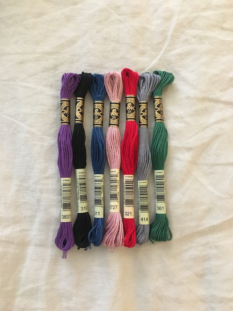 Images shows examples of the embroidery thread color options. From left: Purple, Black, Blue, Pink, Red, Gray, Green.