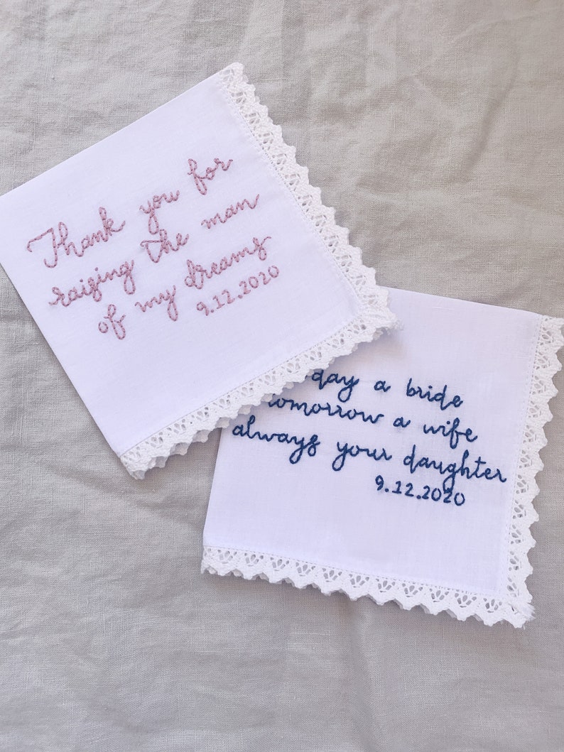 Image shows a white handkerchief with a detailed edge, folded into quarters. The text is the standard message for this listing, with a date added on, in pink thread. Another hankie from a different listing is also in the photo.