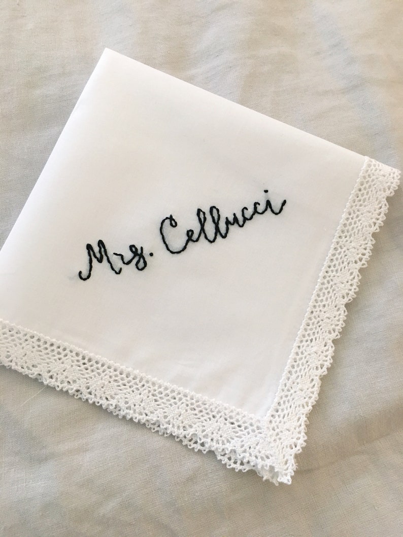 Image shows a white handkerchief with a detailed edge, folded into quarters. The text shows "Mrs. Cellucci", embroidered in black thread.