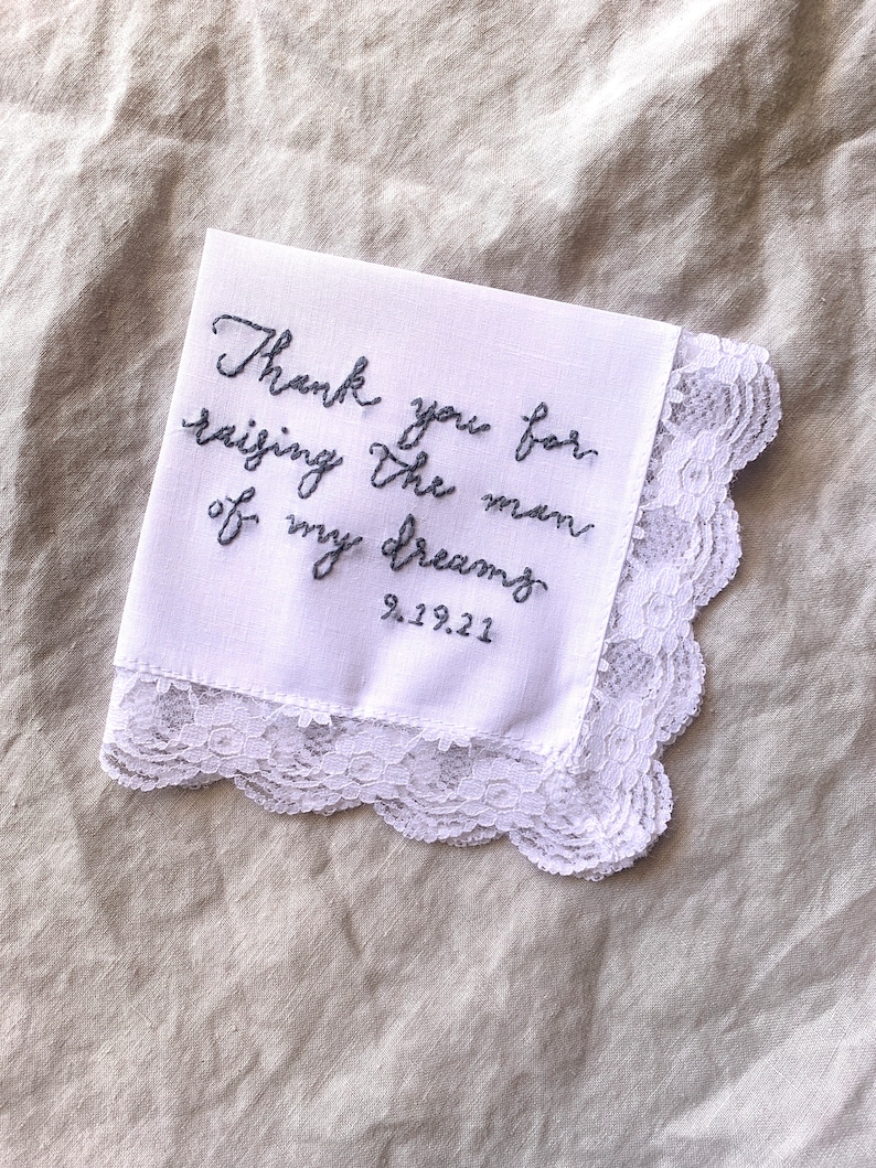 Image shows a white handkerchief with a detailed edge, folded into quarters. The text is the standard message for this listing, with a date added on, in greay thread.