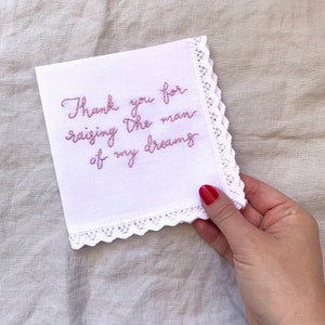 Image shows a white handkerchief with a detailed edge, folded into quarters. The text is the standard message for this listing, in pink thread.