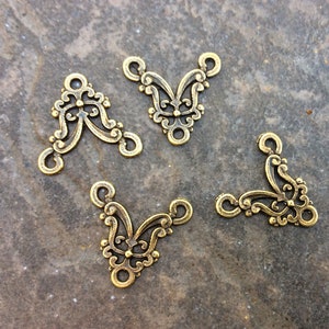 May include: Four gold-toned metal corner connectors with a decorative floral design. Each connector has three holes for attaching to other jewelry pieces.