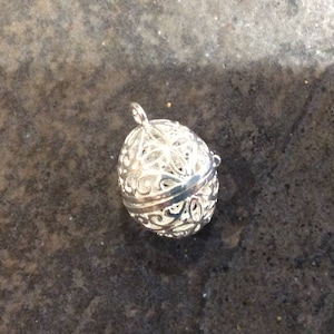 May include: A silver filigree charm in the shape of an egg. The charm is open and has a delicate design.