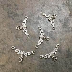 May include: Six silver-toned metal connector charms with a floral design. Each charm has three loops for attaching to jewelry or other crafts.