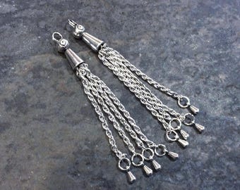 May include: A pair of silver-toned metal tassel pendants featuring a decorative top cap with a small loop. Each pendant consists of multiple twisted rope-style chains hanging down, ending in small, smooth, teardrop-shaped metal charms.