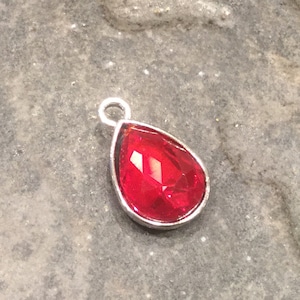 May include: A teardrop-shaped pendant with a red crystal set in a silver frame.